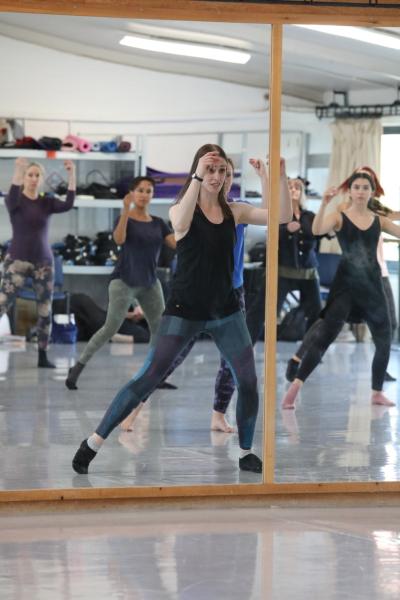 A dance teacher teaching a class of adult students in front of a mirror.
