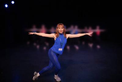 Dancer wearing tap shoes and a blue ISTD lanyard poses with arms outstretched at 90 degrees, and one foot behind the other.